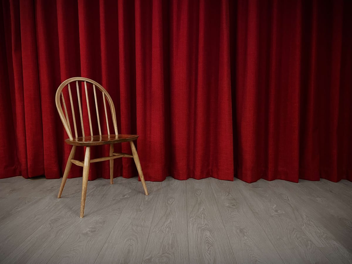 An empty mid-century chair in front of red curtains